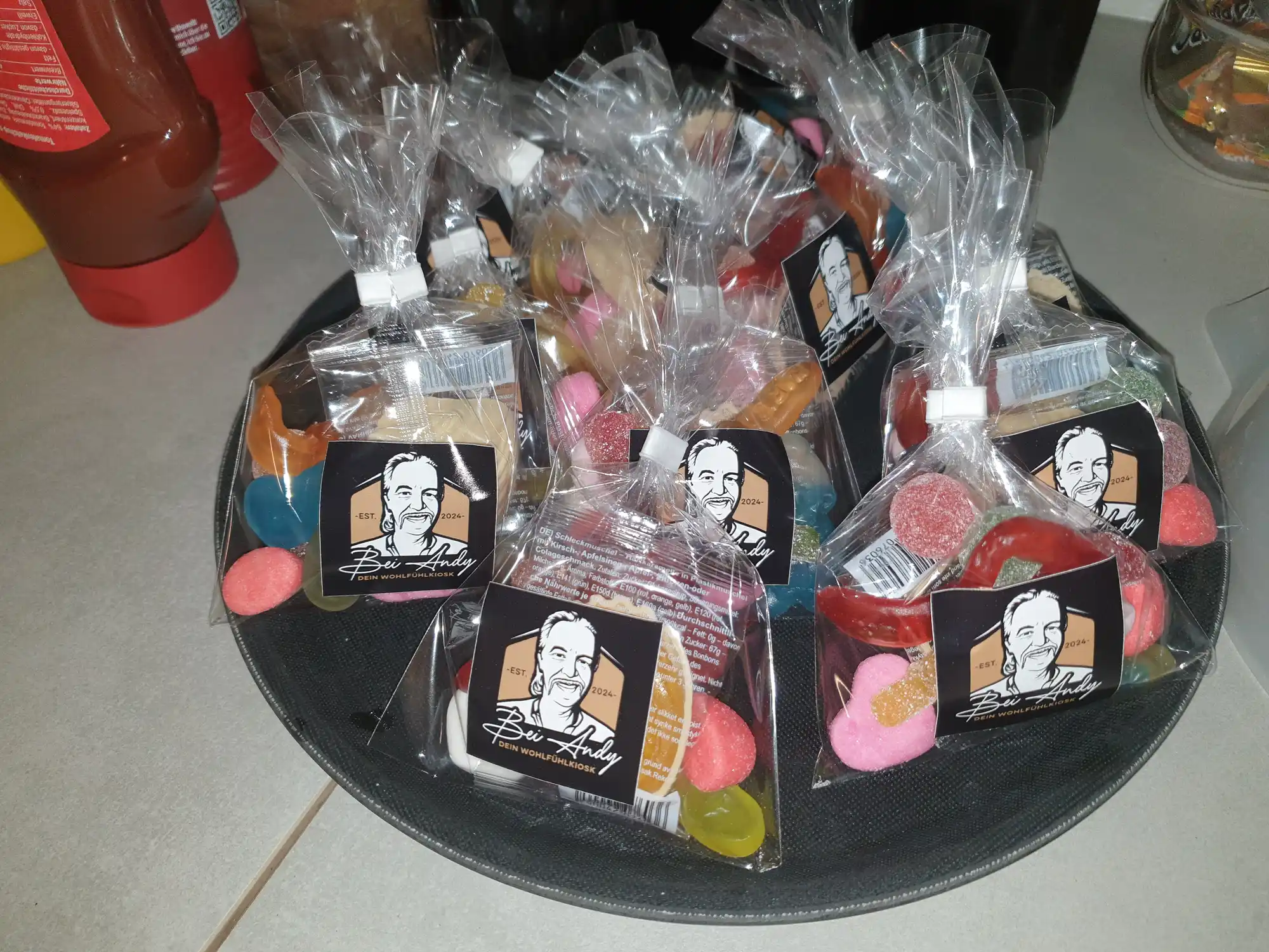 Bunte Eistüten und Süßigkeiten mit Andy-Branding in Folienbeuteln auf schwarzem Tablett im Kaffeegarten Bei Andy in Lübeck